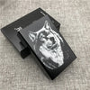 A black cigarette case with an engraved wolf head design on the lid, resting on a gray textured surface.