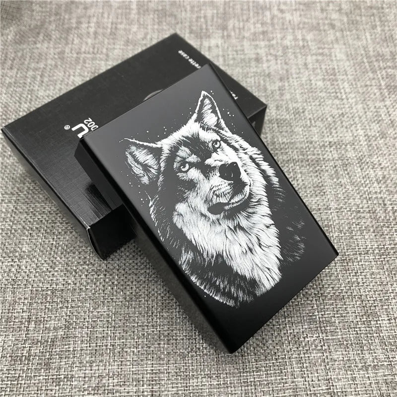 A black cigarette case with an engraved wolf head design on the lid, resting on a gray textured surface.