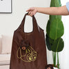 Un sac de shopping en cuir marron avec un dessin de ours de dessin animé encadré en or, tenu par une main.