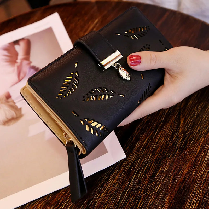 Clutch cartera de cuero PU negro con detalles en hoja de oro, sostenida por una mano sobre una mesa de madera.