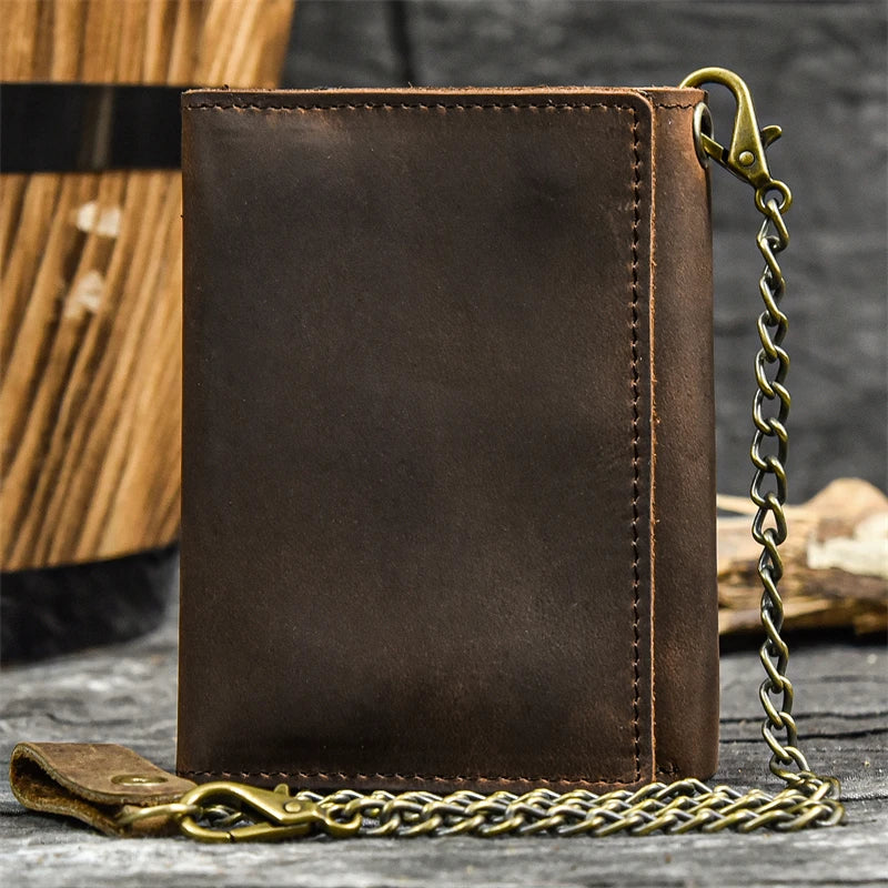 A dark brown genuine leather trifold wallet with a brass chain attached, resting on weathered wood.