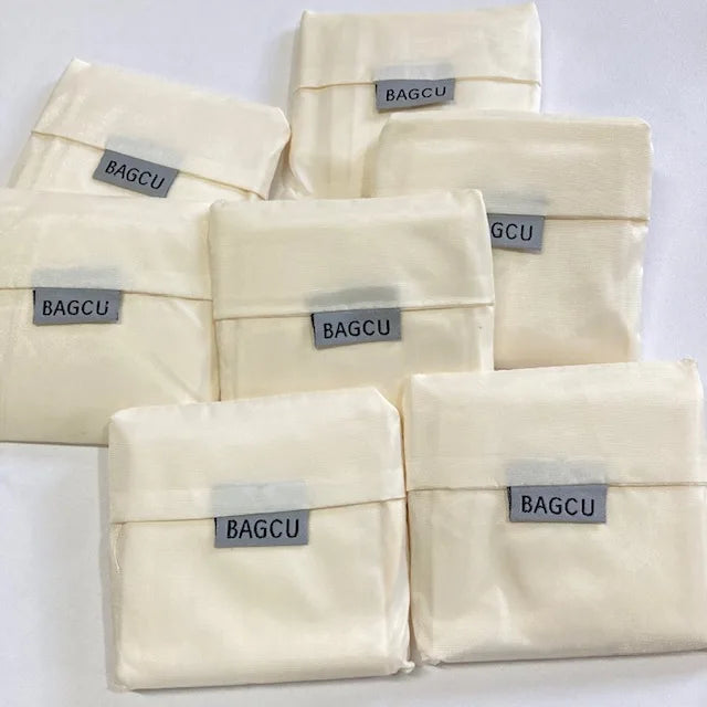 Several light beige eco-friendly foldable shopping bags are stacked and laid out.