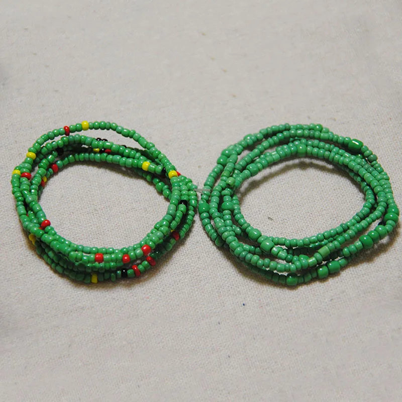 Two strands of colorful green and red belly bead chains laid out on a light background.