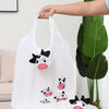 Un sac de shopping blanc avec un dessin de vache noir et blanc tenu par une main.