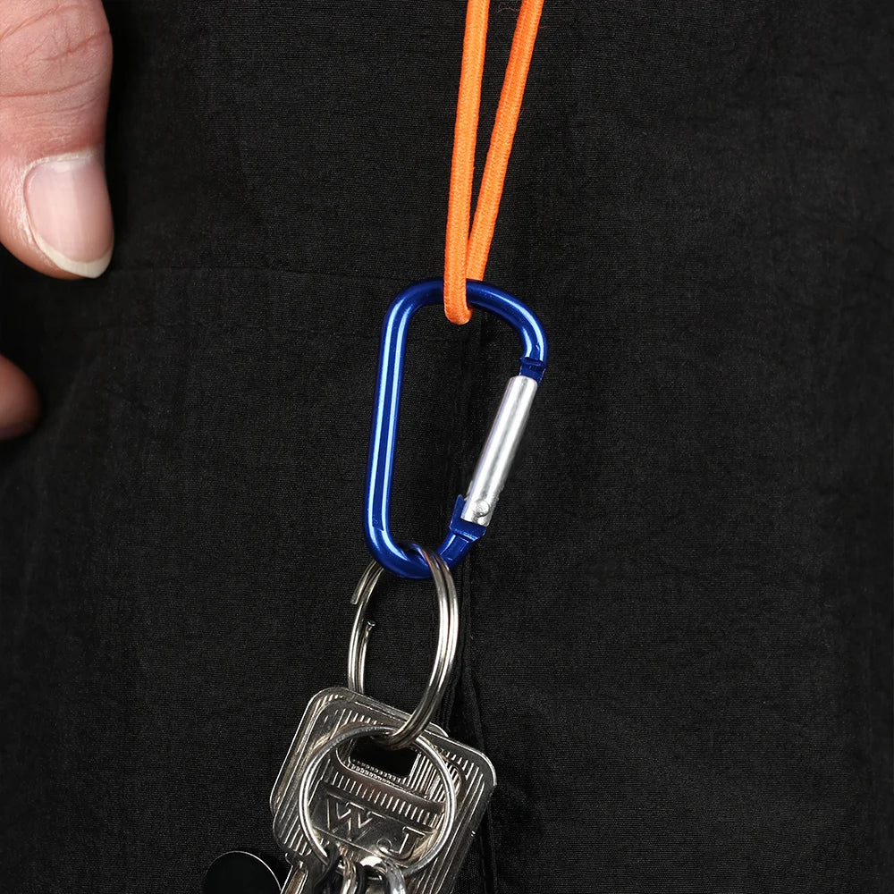 A close-up of a durable aluminum carabiner key ring attached to an orange cord, held by a hand against a black fabric.