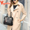A woman models a beige trench coat and a black crocodile-embossed leather tassel shoulder bag.