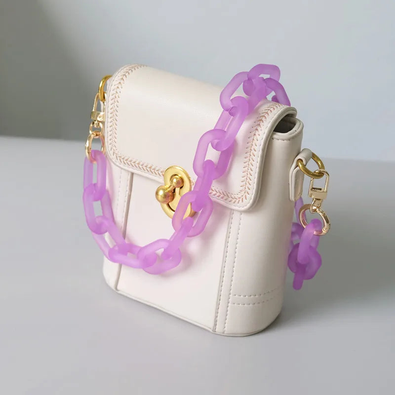 A light pink leather shoulder bag with a gold chain strap and purple chain accents.