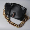 Bolso de hombro de resina negra con correa de cuero y cadena dorada.