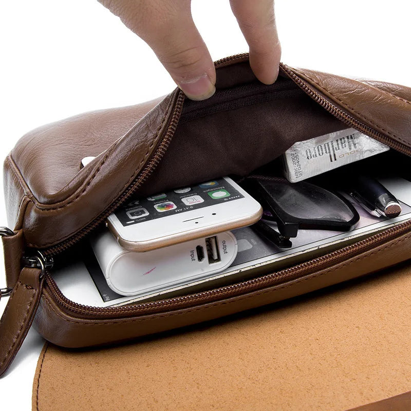 A hand opens a brown retro PU leather crossbody shoulder bag revealing a smartphone and sunglasses inside.