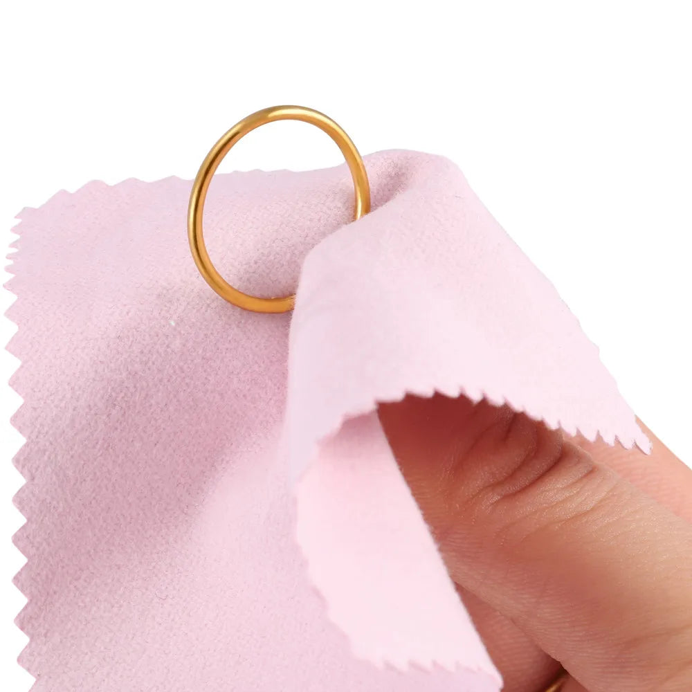 A gold ring is shown resting on a pink polishing cloth.