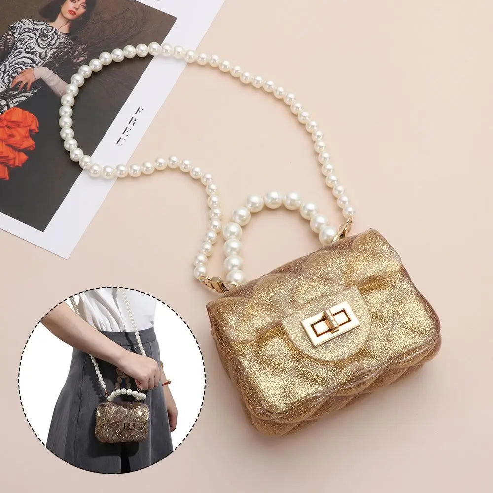 A golden glitter clutch purse is shown with a pearl strap, resting on a light pink background.