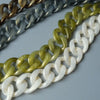 Primer plano de tres cadenas de hombro de resina ajustable en tonos dorado, gris y verde, dispuestas en diagonal sobre una su