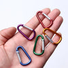 A hand holds several colorful aluminum carabiner key rings with metal split rings.