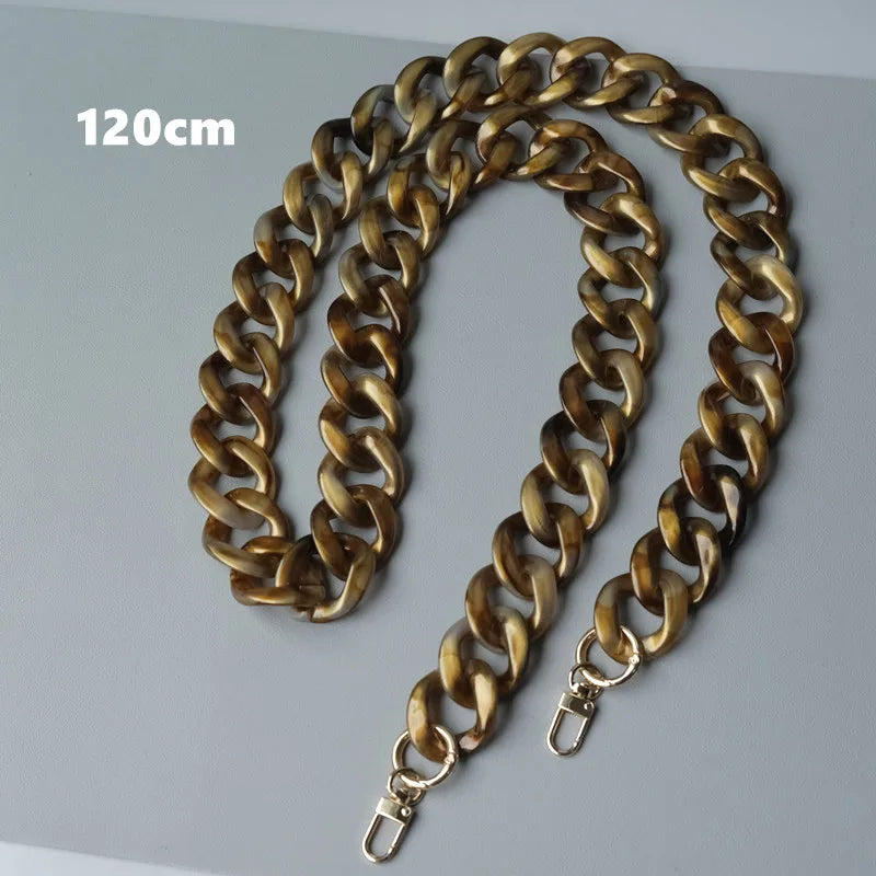 Un bolso de cadena de hombro de resina dorada y larga, exhibido contra un fondo gris claro.
