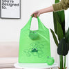 Un sac de courses réutilisable vert lime avec un dessin de grenouille de dessin animé, tenu par une personne.
