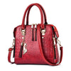 A red crocodile-embossed leather tassel shoulder bag with gold hardware.