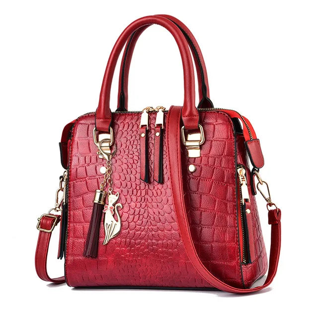 A red crocodile-embossed leather tassel shoulder bag with gold hardware.