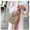A woman holds a handwoven straw moon bag with a top handle while wearing a pink striped dress.