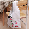 Un sac de shopping blanc avec un motif de vache noire et rose posé sur une chaise en bois.