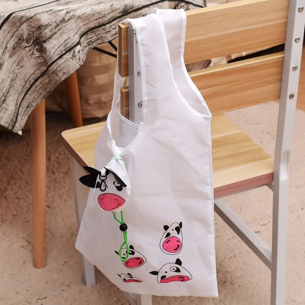 Un sac de shopping blanc avec un motif de vache noire et rose posé sur une chaise en bois.