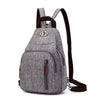 A gray canvas backpack with brown straps and zippers is shown from the back.