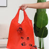 Une main tient un sac de shopping orange vif avec un dessin d'insecte cartoon noir sur fond clair.