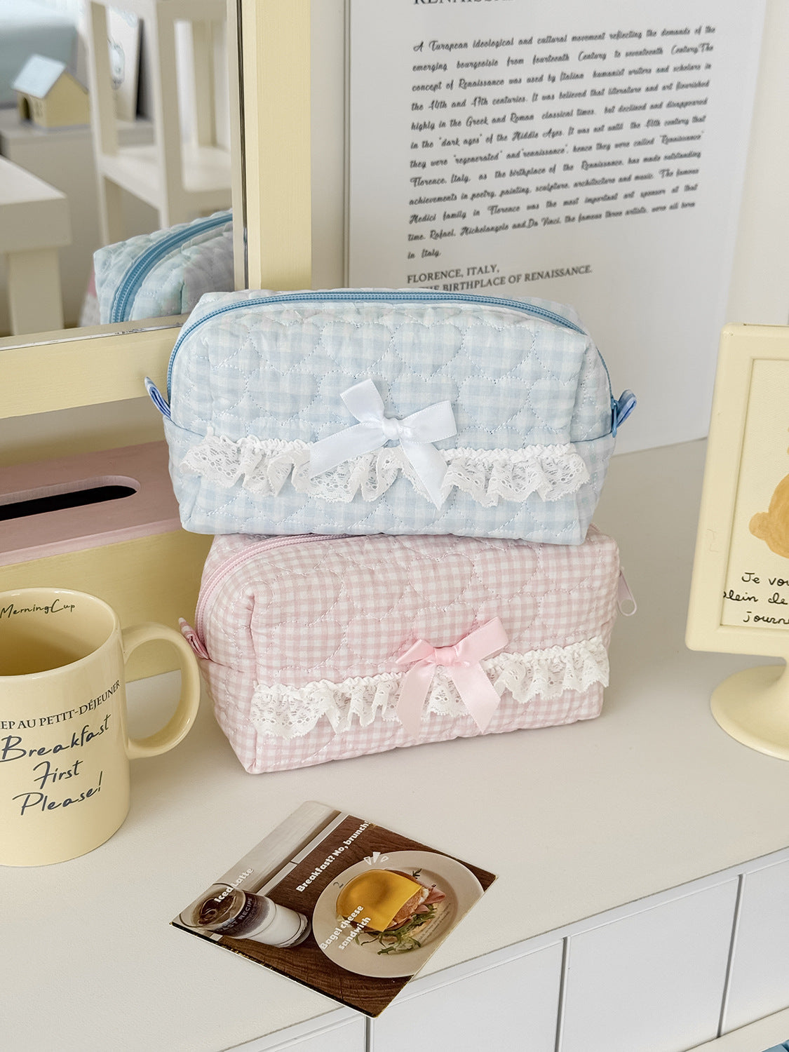 A pink rose sweetheart cosmetic storage pouch is displayed on a white surface next to a mug and a piece of food.