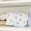 A white cosmetic storage pouch with lace trim and blue floral embroidery rests on a white shelf next to a clock.