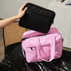 A hand is holding a black travel duffle bag above a pink duffel bag resting on a black marble surface.