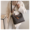 A woman wearing a cream cardigan holds a brown leather crossbody tote bag with a monogram pattern.