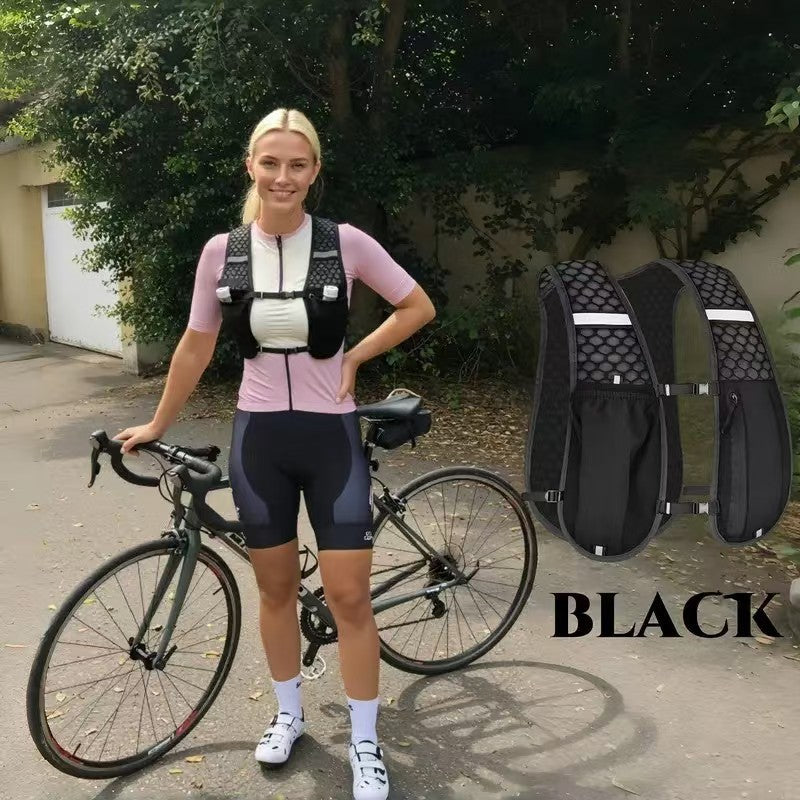 A woman wearing a pink shirt and black cycling shorts stands next to a black hydration vest backpack and a bicycle.