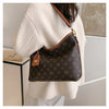 A woman is holding a brown leather crossbody tote bag with a gold chain against a light colored coat.