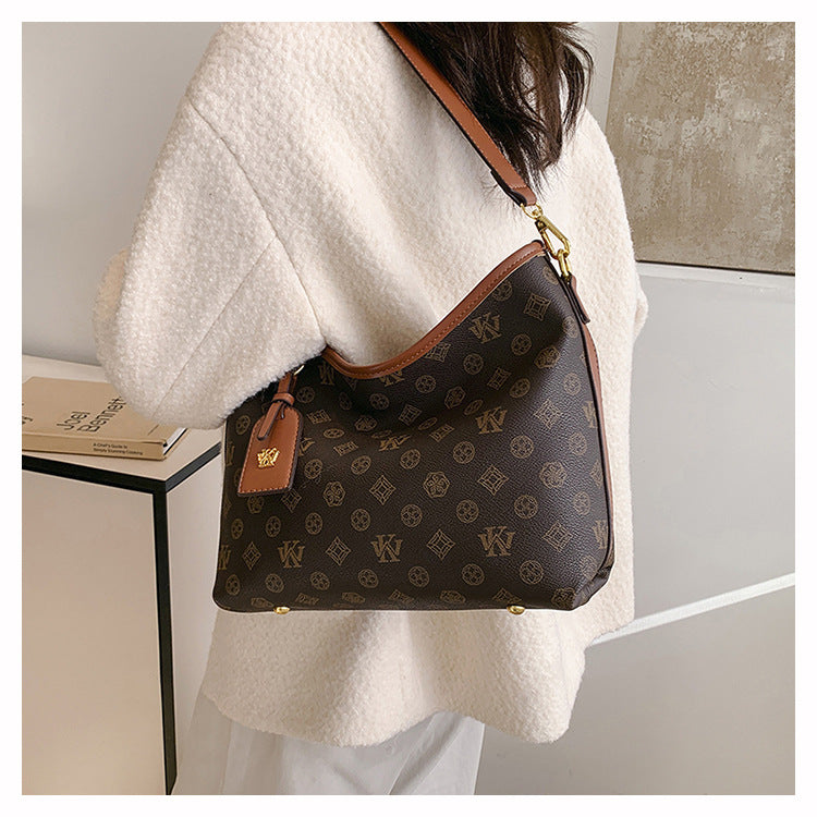A woman is holding a brown leather crossbody tote bag with a gold chain against a light colored coat.