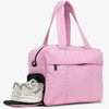 A pink large capacity women's travel duffle bag with a padded shoulder strap and a pair of white sneakers visible.