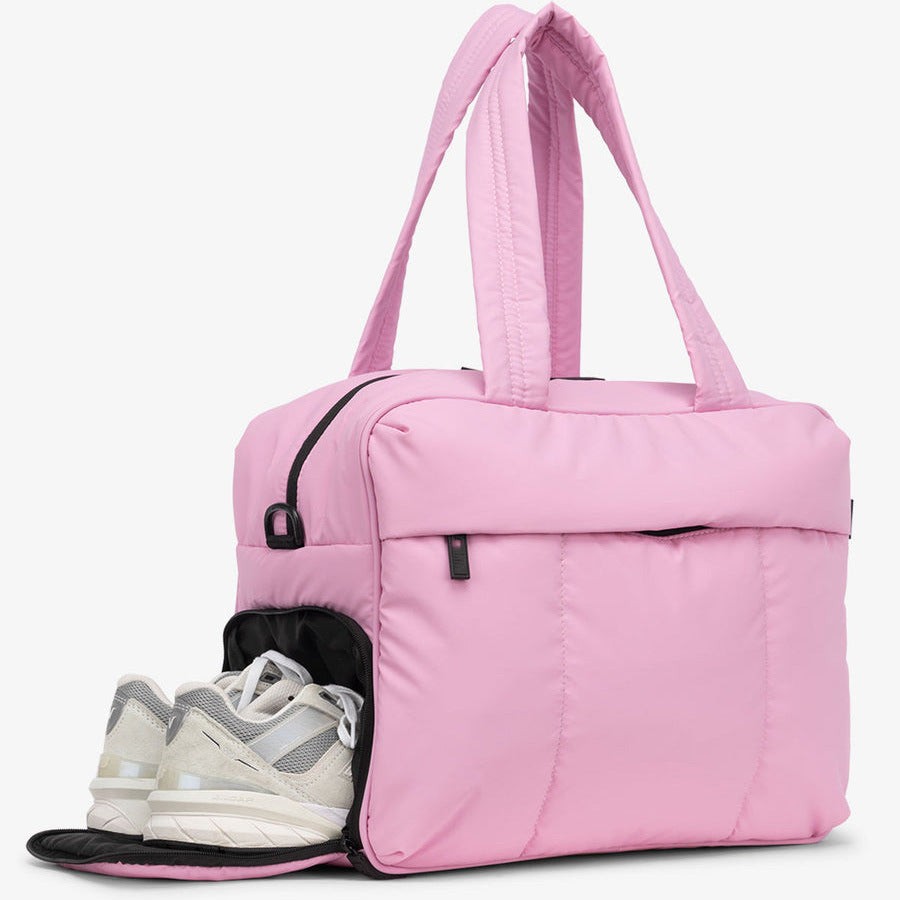 A pink large capacity women's travel duffle bag with a padded shoulder strap and a pair of white sneakers visible.