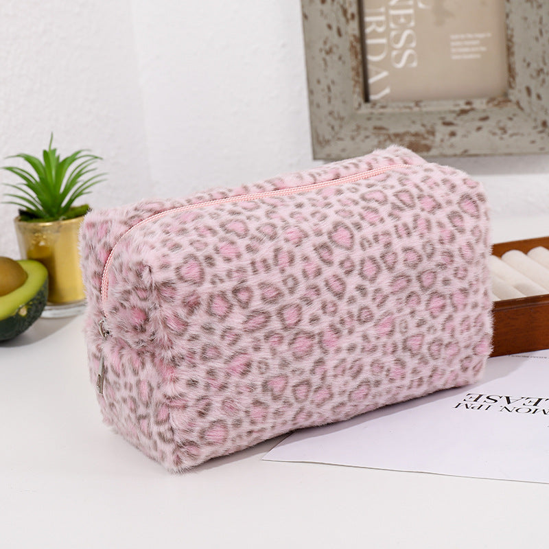 Bolsa organizadora de cosméticos con estampado de leopardo rosa sobre una superficie blanca junto a una planta en maceta y un