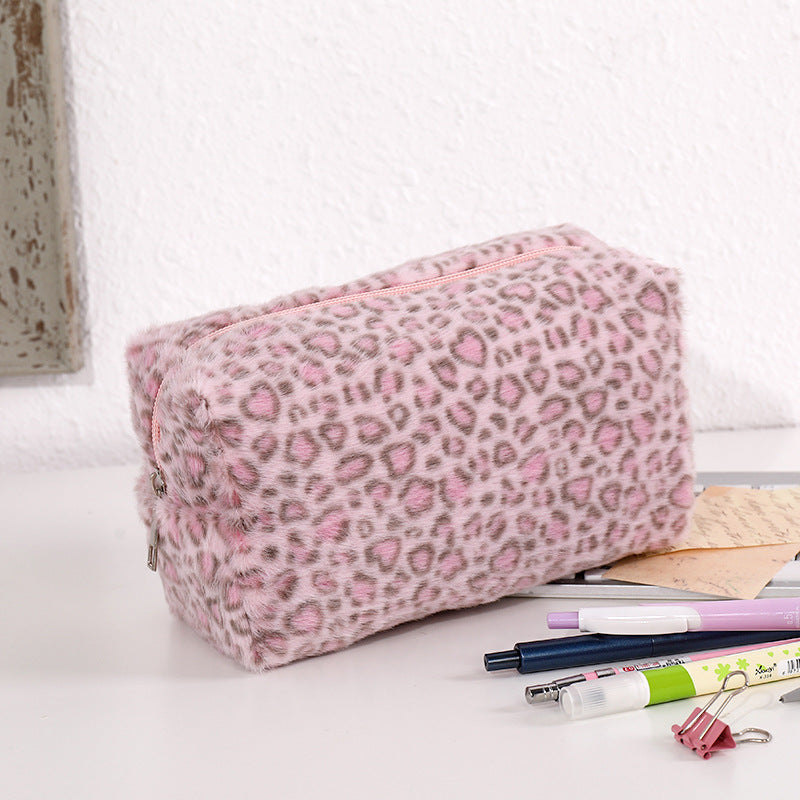 Bolsa organizadora de cosméticos con estampado de leopardo rosa sobre una superficie blanca junto a bolígrafos y herramientas