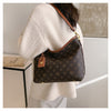 A beige knit sweater sleeve shows a brown leather crossbody tote bag with a dark brown pattern and gold hardware.
