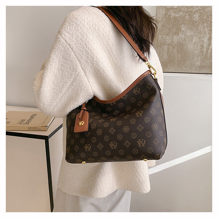 A beige knit sweater sleeve shows a brown leather crossbody tote bag with a dark brown pattern and gold hardware.