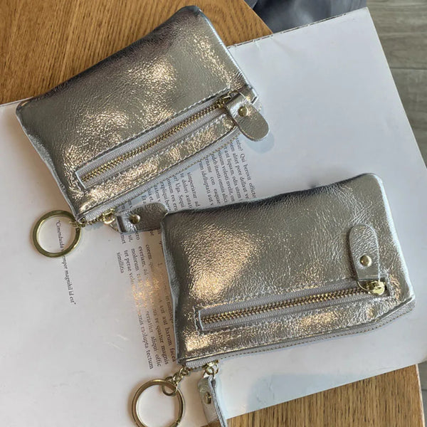 A silver metallic leather compact coin purse and key holder resting on a white sheet of paper.