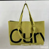 A mustard yellow knitted large tote bag with black lettering and a matching strap.