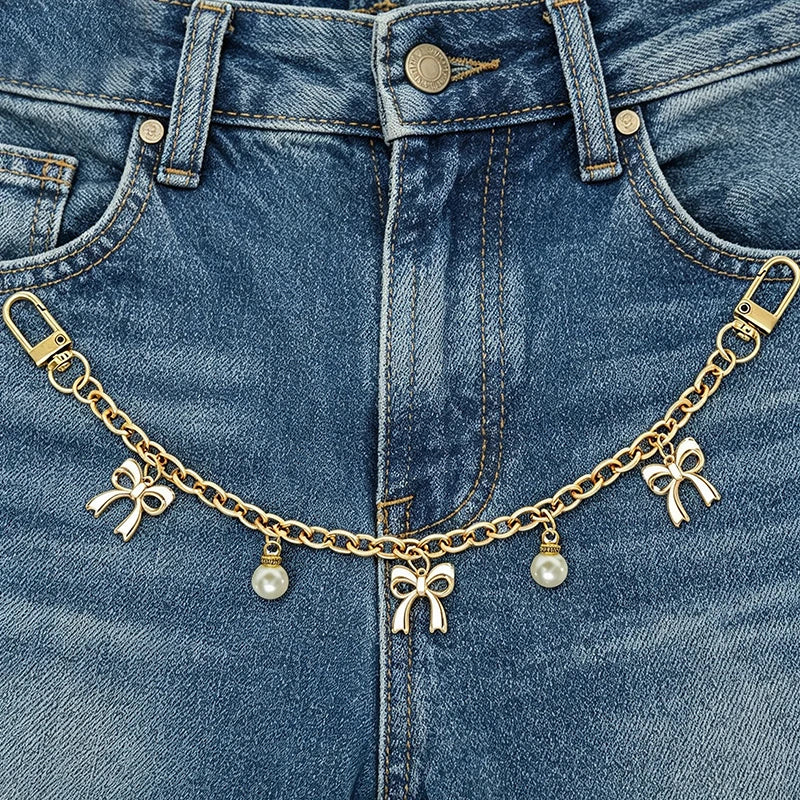 A close-up of a denim jean pocket featuring a gold chain bag with pearl charms.