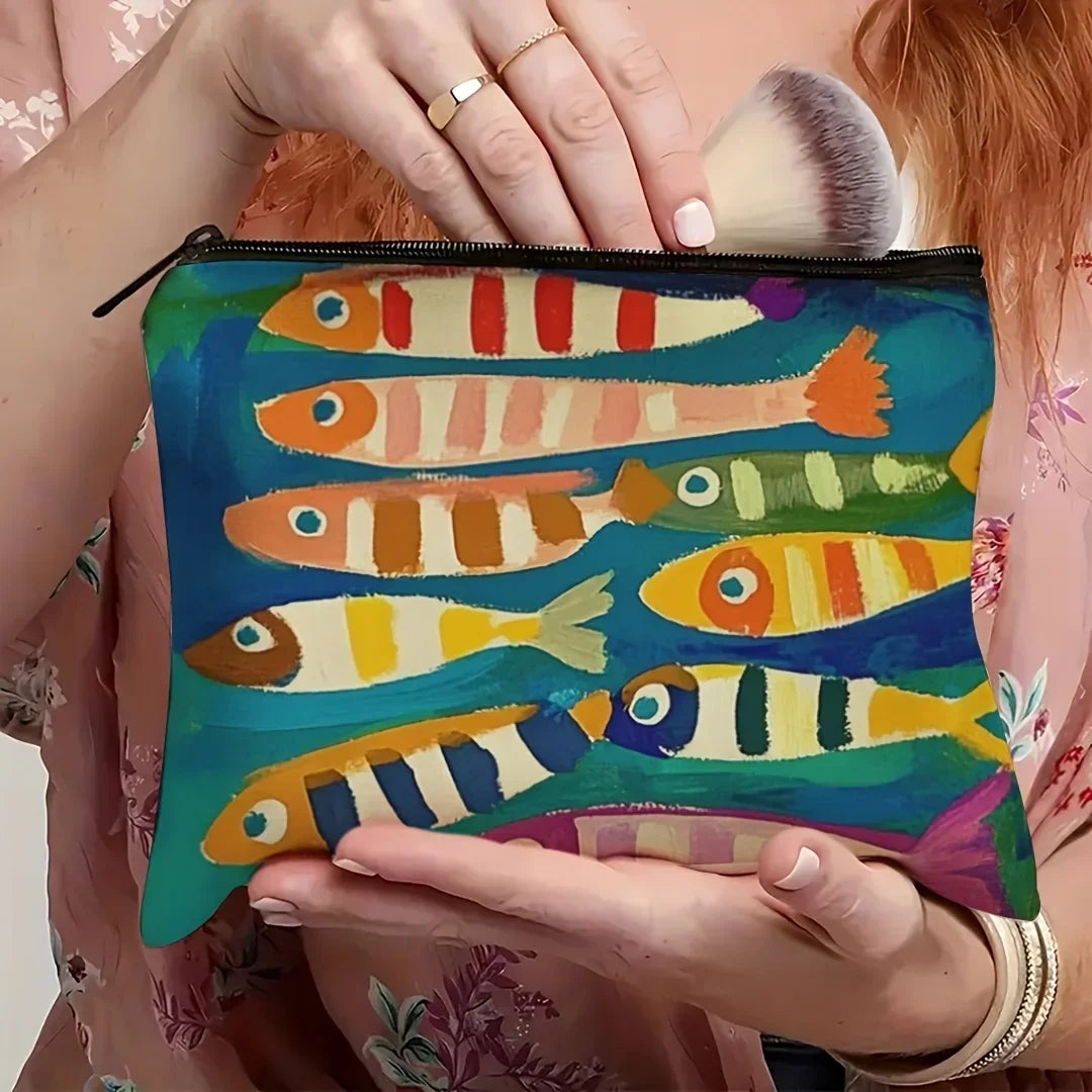 Un sac de maquillage coloré avec des dessins de poissons peints sur un fond bleu sarcelle, tenu par une personne.