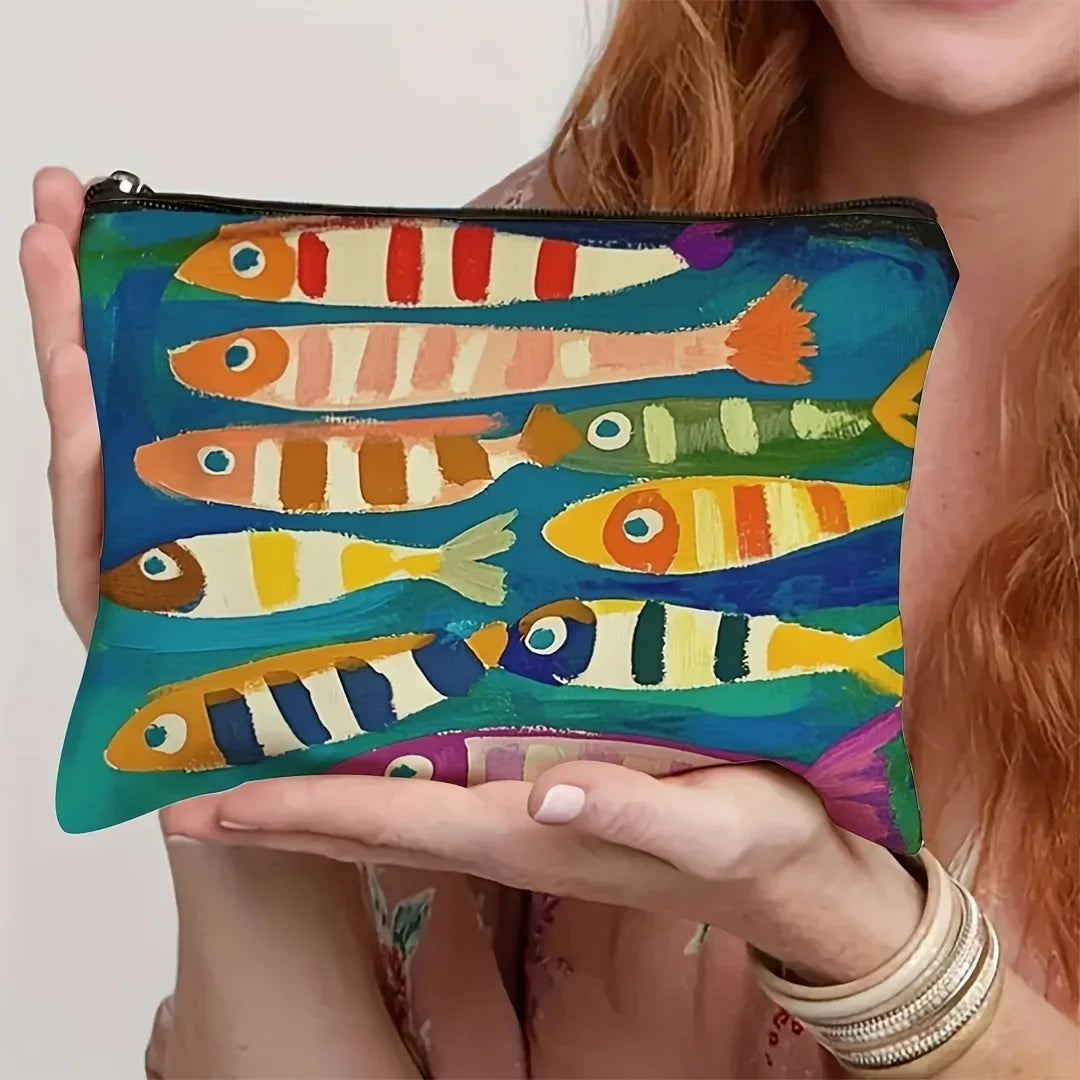 Une main tient un sac cosmétique bleu sarcelle à motif de poisson vintage pour l'organisation des voyages et du maquillage.