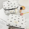 A white quilted makeup bag with black and gold floral embroidery resting on a white surface.