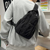 A person wearing a gray sweatshirt is carrying a black versatile casual backpack over their shoulder.