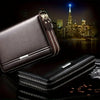 A dark brown leather mens long zipper wallet clutch displayed on a black surface.
