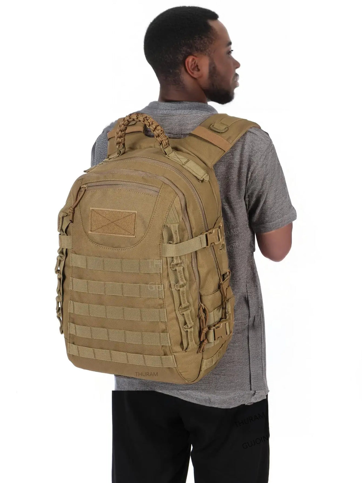 A man wearing a gray shirt is holding a tan tactical waterproof backpack.