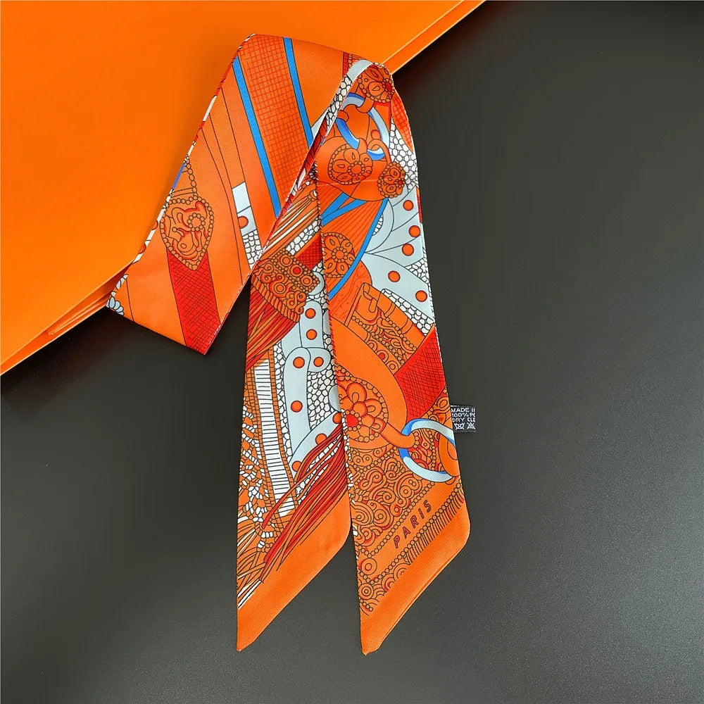 Orange and white patterned silky twill ribbon scarf displayed against an orange background.