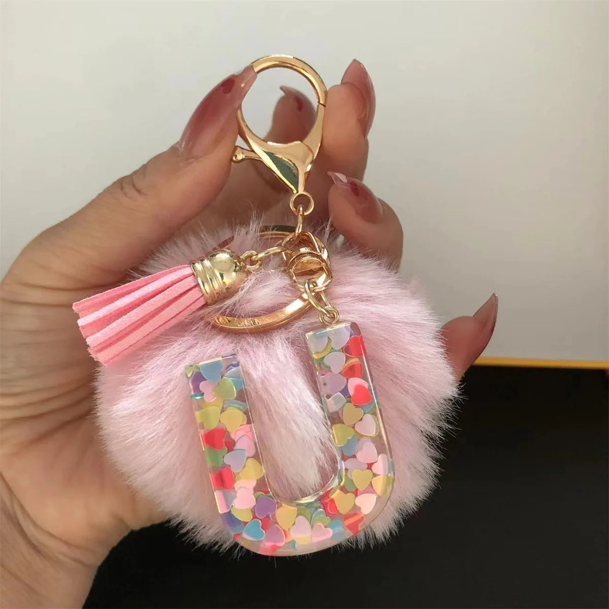 A hand holds a custom initial letter keychain featuring a shiny resin pendant and a pink alphabet charm.